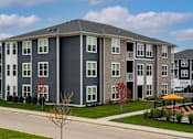 Thumbnail 34 of 35 - Apartment building with grey and white exterior and a small tree in front.