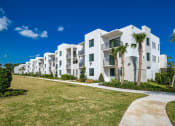 Thumbnail 49 of 78 - a row of white apartment buildings with palm trees in front of them at Altis Blue Lake, Lake Worth, FL