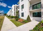 Thumbnail 54 of 78 - a sidewalk in front of a building with grass and plants at Altis Blue Lake, Lake Worth, 33467