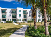 Thumbnail 52 of 78 - an apartment building with a sidewalk and palm trees at Altis Blue Lake, Lake Worth, Florida