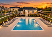 Thumbnail 22 of 25 - A large swimming pool surrounded by lounge chairs and a building in the background.
