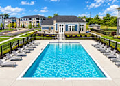 Thumbnail 21 of 25 - A large swimming pool surrounded by lounge chairs and a building in the background.