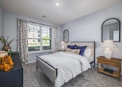 Thumbnail 3 of 16 - A bedroom with a large bed, a nightstand, and a window with curtains.