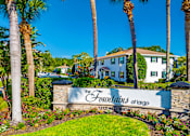 Thumbnail 1 of 10 - The entrance to The Fountains of Largo, a gated community with white houses and palm trees.