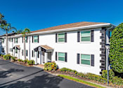 Thumbnail 9 of 10 - A white building with black shutters and a brown roof.