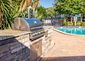Thumbnail 7 of 10 - A silver barbecue grill is on a stone wall next to a pool.
