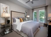 Thumbnail 13 of 47 - Dog-Friendly Luxury Apartments In Atlanta, GA - Venue Brookwood - Spacious Bedroom With Carpet Flooring, Large Bed, Multi-Level Nightstands With Lamps, Ceiling Fan, Dresser, Chair, And Large Windows.