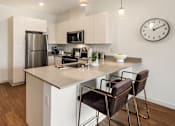 Thumbnail 2 of 27 - SE Redmond, WA, Apartments Near Redmond Town Center - The Bond - Kitchen with Breakfast Bar, Stainless Steel Appliances, White Cabinetry, and Vinyl Plank Hardwood Flooring.
