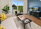 Thumbnail 3 of 27 - Dog-Friendly Apartments in SE Redmond, WA - The Bond - Living Room with Vinyl Plank Hardwood Flooring, Couch, Coffee Table, Armchair, Media Console, TV, Lamp, and a Glass Door leading to the Balcony.