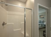 Thumbnail 37 of 37 - A white bathroom with a glass shower door and a bedroom visible through the door.