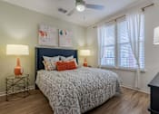 Thumbnail 7 of 25 - 2-Bedroom Apartments in Tampa, FL - Havana Square - Bedroom with Vinyl Plank Flooring, Large Bed, Nightstands with Lamps, Wall Art, Ceiling Fan, Dresser with Lamp, and Large Window with Coverings.