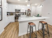 Thumbnail 2 of 25 - 1-Bedroom Apartments in Tampa, FL - Havana Square - Kitchen with Vinyl Plank Flooring, Granite Countertops, Designer Cabinetry, Tile Backsplash, Stainless Steel Appliances, Kitchen Island with Bar-Stool Seating, and Pendant Lights.