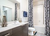 Thumbnail 20 of 40 - A bathroom with a white toilet, a sink, and a shower with a black and white curtain.