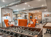 Thumbnail 28 of 40 - A foosball table is in the middle of a room with orange chairs and a stone wall.