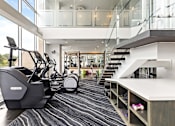 Thumbnail 57 of 72 - A gym with a treadmill, elliptical machines and a staircase.