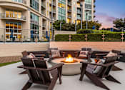 Thumbnail 54 of 72 - Buckhead, GA, Luxury Apartments With In-Unit Washer and Dryer - The Huntley - Outdoor Patio With Fire Pit, Cushioned Adirondack Chairs, and Evening Building Views.