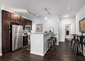 Thumbnail 1 of 26 - A kitchen with a refrigerator, microwave, oven, and bar stools.