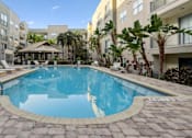 Thumbnail 8 of 27 - Luxury Apartments Near Raymond James Stadium in Tampa, FL - Mosaic Westshore - A large rectangular courtyard pool surrounded by stone pavers, tropical palm trees, and modern lounge chairs.