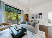 Thumbnail 17 of 28 - A living room with a grey couch, a coffee table, and a large window with a view of trees.