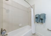 Thumbnail 24 of 28 - A white bathroom with a white tub and a white shower curtain.