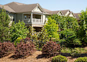 Thumbnail 47 of 48 - A house with a brown roof and a balcony surrounded by green trees and bushes.
