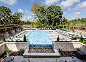 Thumbnail 14 of 34 - A large outdoor swimming pool surrounded by trees and lounge chairs.