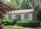 Thumbnail 18 of 27 - A small white house with a green door and window is surrounded by greenery.