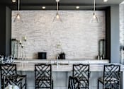 Thumbnail 10 of 53 - A kitchen with a white brick wall and black chairs.