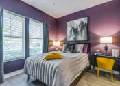 Thumbnail 19 of 35 - 1 BR Luxury Apartments in Altamonte Springs FL - Nine12 Gateway - Furnished Bedroom with Wood-Style Vinyl Plank Flooring, Bed, Nightstand with Lamp, Desk with Yellow Chair and Lamp, Two Windows with Curtains and Blinds, Purple Walls, and Framed Art