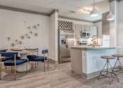 Thumbnail 16 of 29 - Two-Bedroom Luxury Apartments In Sarasota, FL - Botanic Waterside - Kitchen With Wood-Finish Flooring, Stainless Steel Appliances, Dining Table And Chairs, And Counter With Seating And Pendant Lighting.