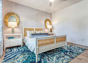 Thumbnail 18 of 29 - 1-Bedroom Luxury Apartments In Sarasota, FL - Botanic Waterside - Bedroom With Wood-Finish Flooring, Colorful Area Rug, Large Bed, Nightstands With Lamps, Wall-Mounted Mirror, Accent Wall, And Ceiling Fan.