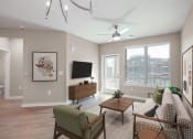 Thumbnail 6 of 32 - Mt. Juliet, TN Apartments Near Percy Priest Lake - The Enclave at Providence - Living Room with Hardwood-Style Flooring, Area Rug, Sofa, Armchair, Coffee Table, Media Cabinet, Wall-Mounted TV, Ceiling Fan, Large Window, and Glass Door with Access to Balcony.