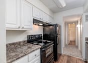 Thumbnail 14 of 35 - A black fridge and stove in a kitchen with white cabinets.