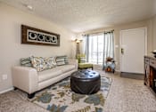 Thumbnail 9 of 30 - A living room with a beige couch, a round ottoman, and a floral rug.