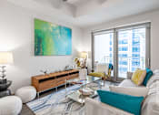 Thumbnail 16 of 36 - A living room with a large painting on the wall and a view of a cityscape through the windows.