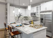 Thumbnail 14 of 36 - Luxury Apartments in Midtown Atlanta, GA with In-Unit Washer and Dryer  - Trace Midtown - Kitchen With White Cabinetry, Stainless Steel Appliances, Granite Countertops, Tile Backsplash, and Island with Pendant Lights and Bar Seating.