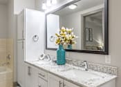 Thumbnail 18 of 36 - A bathroom with a white vanity and a blue vase with flowers.