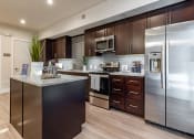 Thumbnail 9 of 35 - Pet-Friendly Apartments in Altamonte Springs, FL - Nine12 Gateway - Kitchen with Vinyl Plank Flooring, Island, Quartz Countertops, Stainless Steel Appliances, and Dark Brown Cabinetry.