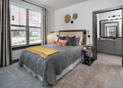 Thumbnail 10 of 46 - Duluth, GA, Apartments Near Stone Mountain Park - District at Duluth - Bedroom with Carpeted Floor, Bed, Nightstands with Lamps, Oversized Window, and Attached Bathroom.