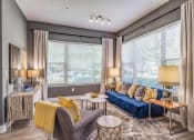 Thumbnail 17 of 35 - Altamonte Springs, FL Luxury Apartments - Nine12 Gateway - Furnished Living Room with Wood-Style Vinyl Plank Flooring, Area Rug, Sofa, Armchair, Cofeetable, Side Tables with Lamps, Storage Dresser with Wood-Style Design, and Two Large Windows with Blinds and Curtains