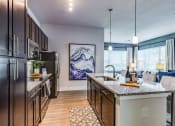 Thumbnail 16 of 35 - Luxury Apartments for Rent in Altamonte Springs, FL - Nine12 Gateway - Modern Kitchen with Wood-Style Vinyl Plank Flooring, Dark Wood Cabinetry, Large Cooking Island with Sink and Bar Chairs, Pendant Lights, Granite Countertops, and Stainless Steel Appliances