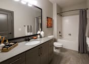 Thumbnail 16 of 46 - Duluth, GA, Apartments Near Mercedes-Benz Stadium - District at Duluth - Bathroom with Tile Floor, Garden-Style Tub, Quartz Vanity Countertop, Large Mirror, and Wood-Tone Cabinets.