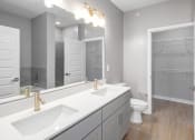 Thumbnail 19 of 32 - Mt. Juliet TN Apartments - The Enclave - Bathroom with Hardwood-Style Flooring, Double Sinks, Granite Countertop, Large Vanity Mirror, and Spacious Walk-In Closet with Storage Shelves