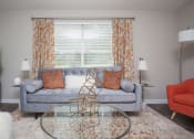 Thumbnail 8 of 16 - Dog-Friendly Apartments in Atlanta, GA - City Park - Living Room with Modern Wood-Style Flooring, Area Rug, Couch, Armchair, Glass-Top Coffee Table, End Tables with Lamps, Floor Lamp, and Large Window.