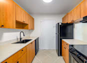 Thumbnail 5 of 22 - A kitchen with wooden cabinets and black appliances.