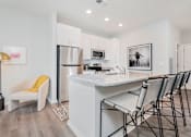 Thumbnail 2 of 49 - Luxury Apartments in Louisville, KY, with In-Unit Washer and Dryer - The Laurel Apartments - Kitchen With White Cabinetry, Stainless Steel Appliances, Granite Island Seating, And A Cozy Accent Chair.