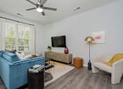 Thumbnail 18 of 49 - One Bedroom Luxury Apartments In Jeffersonville, IN - The Laurel - Living Area With Wood-Style Floor, Large Window, Sofa, Armchair, Coffee Table, Wall-Mounted TV, And Ceiling Fan.