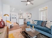 Thumbnail 1 of 14 - Lebanon, OH, Luxury Apartments For Rent - Founders Landing - A Modern Living Area With A Blue Velvet Sofa, A Gold Floor Lamp, And A White Kitchen Island In An Open-Concept Layout.