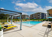 Thumbnail 46 of 49 - Luxury Apartments with Attached Garage in Louisville, KY - The Laurel Apartments - Swimming Pool With Lounge Chairs, Blue Umbrellas, Covered Seating, Apartment Buildings, And A Bright Sky.