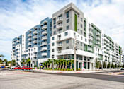 Thumbnail 1 of 18 - A modern apartment building with a red car parked in front.